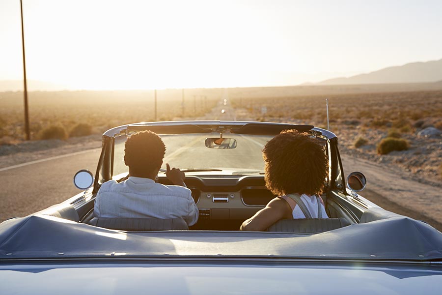 About Our Agency - Couple Cruising In Their Convertible On a Dessert Road at Dusk